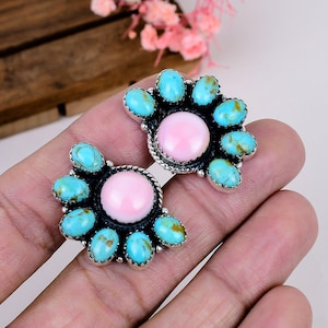 May include: A pair of silver earrings featuring a central round pink stone surrounded by a cluster of seven oval turquoise stones. The silver settings have a twisted rope texture around the central pink stone and a polished finish.