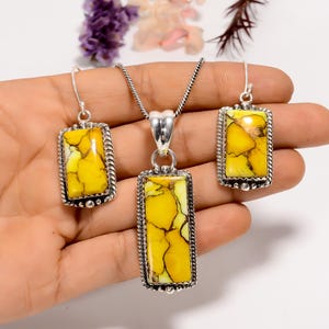 May include: A jewellery set featuring a pendant necklace and matching earrings. The rectangular pendants and earrings have a yellow and brown stone set in a silver-coloured metal frame. The earrings have a hook closure.