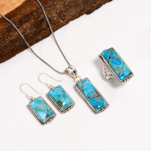 May include: A jewelry set featuring a necklace, earrings, and a ring. Each piece has a rectangular turquoise stone set in a silver-colored metal frame. The turquoise stones have a mottled blue and brown pattern.