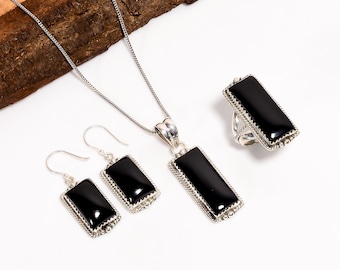 May include: A jewellery set comprising a necklace, earrings, and a ring. Each item features a rectangular black stone set in silver-coloured metal. The earrings are drop style, and the ring has a wide band.