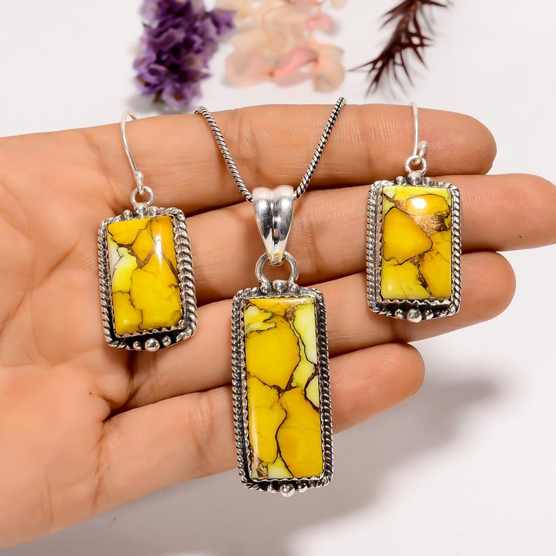 May include: A jewellery set comprising a pendant necklace and matching earrings. The rectangular pendants and earrings feature a yellow and brown stone set in a silver-coloured metal frame with a rope-like border. The necklace has a silver chain.