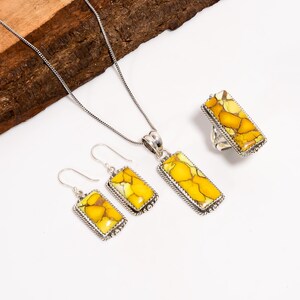 May include: A jewellery set comprising a necklace, earrings, and a ring. Each item features a rectangular yellow and white stone set in silver-coloured metal. The earrings are hook-style, and the ring has a wide band.
