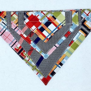 May include: A colorful patchwork bandana with a geometric pattern in shades of red, blue, green, and white. The bandana is made of fabric and has a triangular shape.