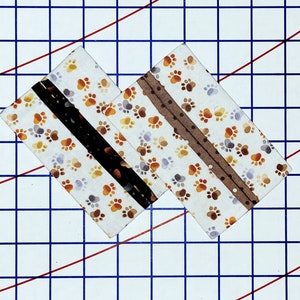 May include: Two white fabric squares with brown paw print patterns. Each square has a brown and black ribbon sewn across the center.
