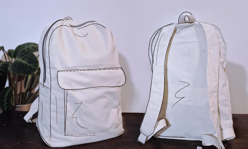 Puede incluir: Dos mochilas blancas con detalles de contorno negro. Una mochila se muestra desde el frente con un bolsillo y una cremallera. La otra mochila se muestra desde la parte posterior con las correas visibles. Las mochilas est&aacute;n sobre una superficie de madera.