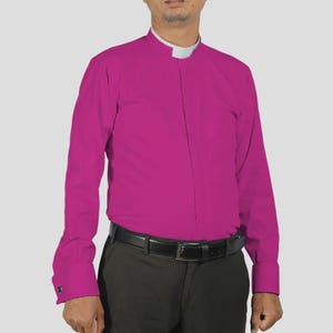 May include: A magenta long-sleeve shirt with a white clerical collar. The shirt is buttoned up and worn with dark gray pants and a black belt. The cuffs are buttoned.