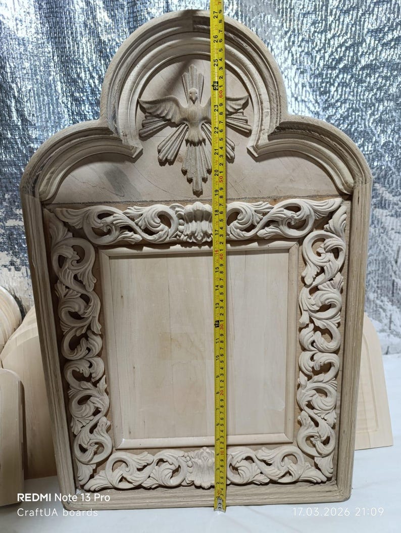 May include: A light-colored, unfinished wooden carving of a religious icon. The carving features a dove with outstretched wings at the top, and ornate scrollwork around the edges. The height is approximately 27 inches.