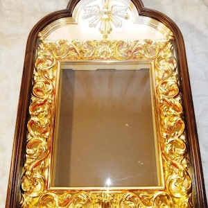 May include: Ornate, rectangular picture frame with a dark brown wooden border and a gold-colored, detailed inner frame. The top of the frame has an arched design with a gold emblem. The frame is empty, ready for a photo or artwork.