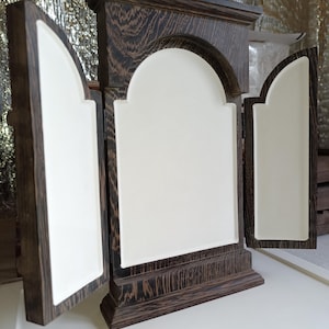 May include: A dark brown wooden cabinet with three arched panels, two of which are open. The panels have a white interior. The cabinet is made of wood with a visible grain pattern. The cabinet is on a white surface.