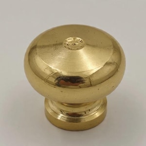 May include: A solid brass cabinet knob with a spherical top and a cylindrical base. The knob has a polished, reflective surface and a classic design. This hardware is suitable for drawers, cabinets, and furniture.