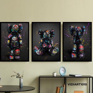 Op de afbeelding: Set van drie ingelijste kunstdrukken met kleurrijke graffiti-achtige berenfiguren tegen een donkergrijze achtergrond. De berenfiguren hebben meerdere kleuren en patronen. Het kunstwerk is zwart omlijst.