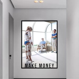 May include: A framed artwork with the text "MAKE MONEY" in bold, black letters. The image shows a person covered in money, standing in front of two other people. The artwork is displayed in a hallway with a white wall and a grey door.