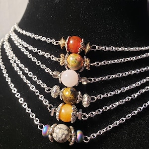Peut inclure: Un collier à plusieurs rangs avec des chaînes argentées et des perles de pierres précieuses colorées. Les perles sont de différentes couleurs, dont le rouge, le vert, le rose, le jaune et le gris. Le collier est présenté sur un mannequin noir.