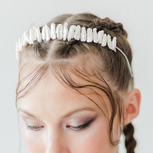 Op de afbeelding: Een vrouw met nat haar dat in twee vlechten is gestyled, draagt een parel kroon haarband. De haarband is gemaakt van een zilveren draadbasis met een rij witte parels.