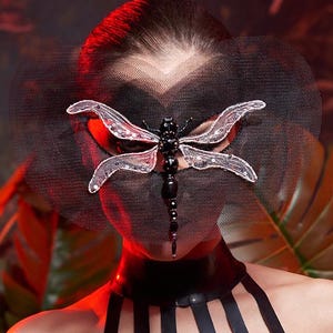 Puede incluir: Top halter de l&aacute;tex negro y m&aacute;scara a juego con dise&ntilde;o de lib&eacute;lula. La m&aacute;scara presenta un velo negro y una lib&eacute;lula decorativa con detalles claros y negros. El fondo tiene follaje rojo y verde.