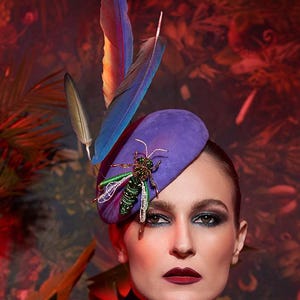 May include: A purple hat with a decorative insect and feather accents. The hat is paired with a matching purple blouse. The background features a dark, leafy pattern with red and green hues, creating a dramatic and stylish look.
