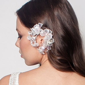 Puede incluir: Un pendiente de oreja floral blanco con pétalos delicados y un acento de perla. El pendiente de oreja se lleva en la oreja izquierda de una persona con el pelo largo y castaño.