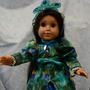 May include: A doll wearing a blue and green peacock-patterned dress with a blue satin skirt and a crown with blue jewels.