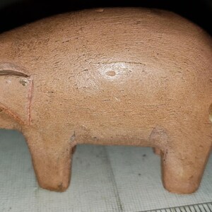 May include: A small, wooden pig figurine with a brown, painted finish. The pig has a curled tail made of twine.