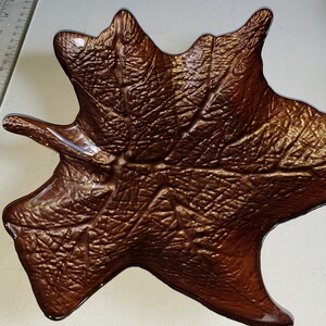 May include: A decorative leaf-shaped dish made of glass with a metallic bronze finish. The dish has a detailed design of veins and ridges, resembling a real leaf.