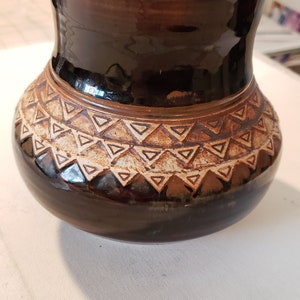 May include: A brown ceramic vase with a geometric pattern of white triangles around the middle.