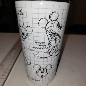 May include: White travel mug featuring a Mickey Mouse sketch design. The mug has a black lid and a grid pattern background. Text includes "Pants Have Pockets" and "Side Ant Arc". The date "7/20/37" is also visible.