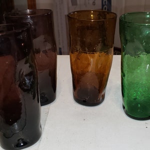 May include: Four glass tumblers in different colors: purple, brown, amber, and green. The glasses have a textured, bumpy surface.