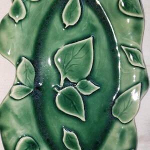 May include: A green ceramic dish with a raised leaf design. The dish is oval shaped and has a glossy finish.