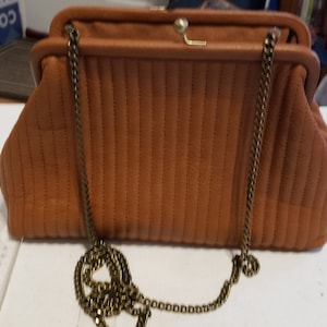 May include: A brown quilted clutch purse with a gold chain strap. The purse has a clasp closure and a quilted design.