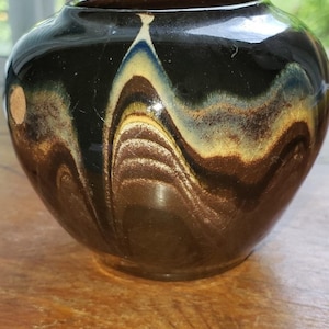 May include: A black ceramic vase with a brown, white, and blue marbled glaze. The vase has a round body and a wide opening.