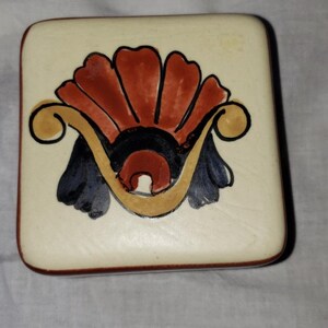 May include: Square ceramic trinket box with a hand-painted design. The design features a stylized floral motif in shades of red, orange, yellow, black, and blue.
