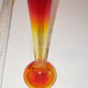 May include: A small, red and yellow glass vase with a flared base. The vase is about 4 inches tall.