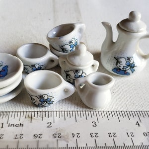 May include: A miniature tea set with a blue and white design featuring a bird with a blue ribbon. The set includes a teapot, creamer, sugar bowl, four cups, and four saucers.