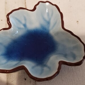 May include: A blue and white ceramic dish with a brown rim, shaped like a flower.