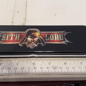 May include: Black rectangular pencil case with the words "Sith Lord" and a Darth Vader graphic. The case is approximately 8 inches long.