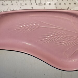 May include: A pink ceramic serving dish with a curved shape and a raised design of wheat stalks.