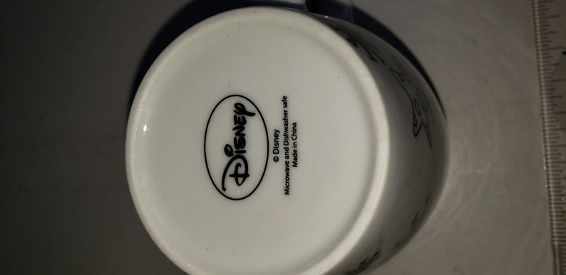 May include: White ceramic mug with a black Disney logo and the text "Microwave and Dishwasher safe. Made in China."