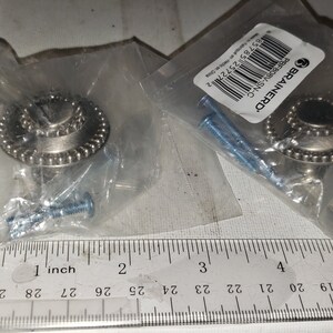 May include: Two silver cabinet knobs with a beaded edge design, packaged in clear plastic. Each knob includes mounting screws. The brand name "BRAINERD" is visible on a label. The knobs are approximately 1 inch in diameter.