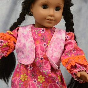 May include: A doll wearing a pink and white vest over a pink dress with a peace sign and flower pattern. The doll has long black hair in braids and brown eyes.