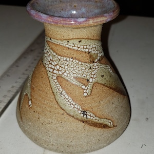 May include: A small, brown ceramic vase with a white crackle glaze and a purple rim. The vase has a rounded body and a narrow neck.