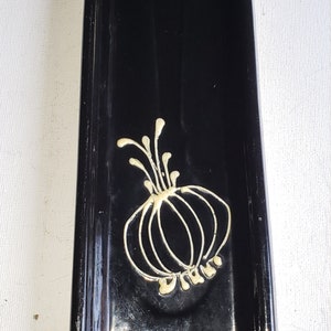 May include: A black ceramic dish with a white floral design. The dish has a wavy edge and is approximately 6 inches long.