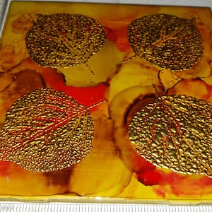 May include: Square tile with four gold leaf leaves on a yellow, orange, and red background.