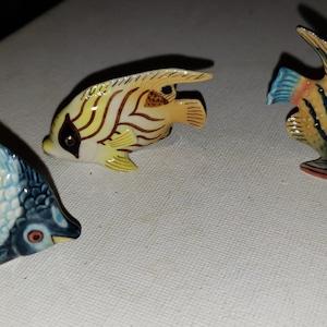 May include: Three ceramic fish figurines with yellow, blue, and white stripes. The fish are painted with realistic details and have a glossy finish.