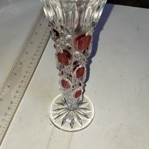 May include: A clear glass vase with a cut glass design and a red glass accent. The vase has a wide mouth and a narrow base.