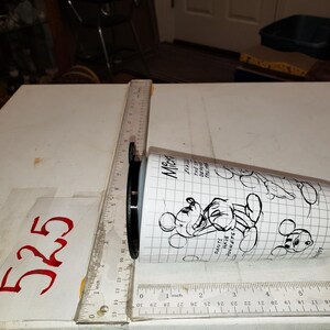 May include: White tumbler with black Mickey Mouse illustrations and text. The tumbler has a black lid and is measured with a ruler. The text on the tumbler includes "Pants have pockets".