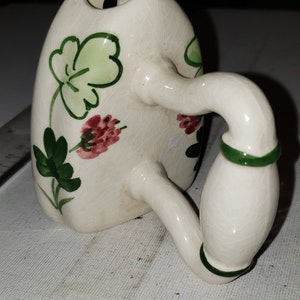 May include: A white ceramic pitcher with a green and pink floral design. The pitcher has a handle and a spout. It is a vintage style pitcher.