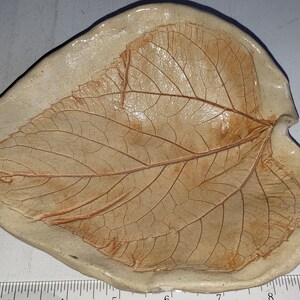 May include: A ceramic leaf-shaped dish with a brown leaf design. The dish is made of white clay and has a rustic look.