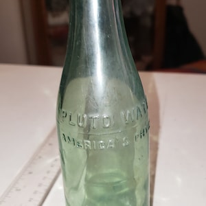 May include: A green glass bottle with the text "Pluto Water America's Phys" on the label.