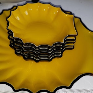 May include: A set of five yellow ceramic bowls with black trim. The bowls are stacked in a spiral shape, creating a unique and decorative display.
