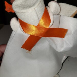 Puede incluir: Un fantasma de fieltro blanco con un sombrero de fieltro marr&oacute;n y una cinta naranja. El fantasma lleva una t&uacute;nica de fieltro blanco.